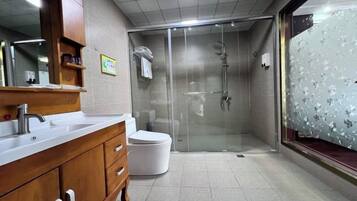 Un baño con tocador de madera, inodoro blanco, ducha con mampara de vidrio y ventana con vidrio esmerilado.