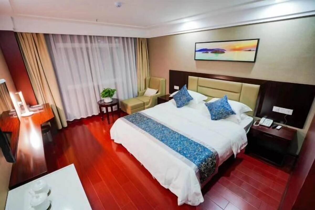 Une chambre d’hôtel avec un grand lit, un bureau, une chaise, une petite table avec une plante et un tableau au mur.