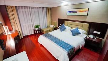 Habitación de hotel con una cama grande, un escritorio, una silla, una mesita con una planta y un cuadro en la pared.