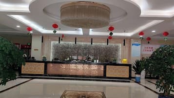 A hotel reception area with a central desk, a chandelier, and potted plants.