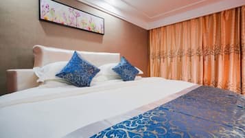 A hotel room with a bed, white headboard, blue patterned pillows, a blue and gold bedspread, and a painting on the wall.