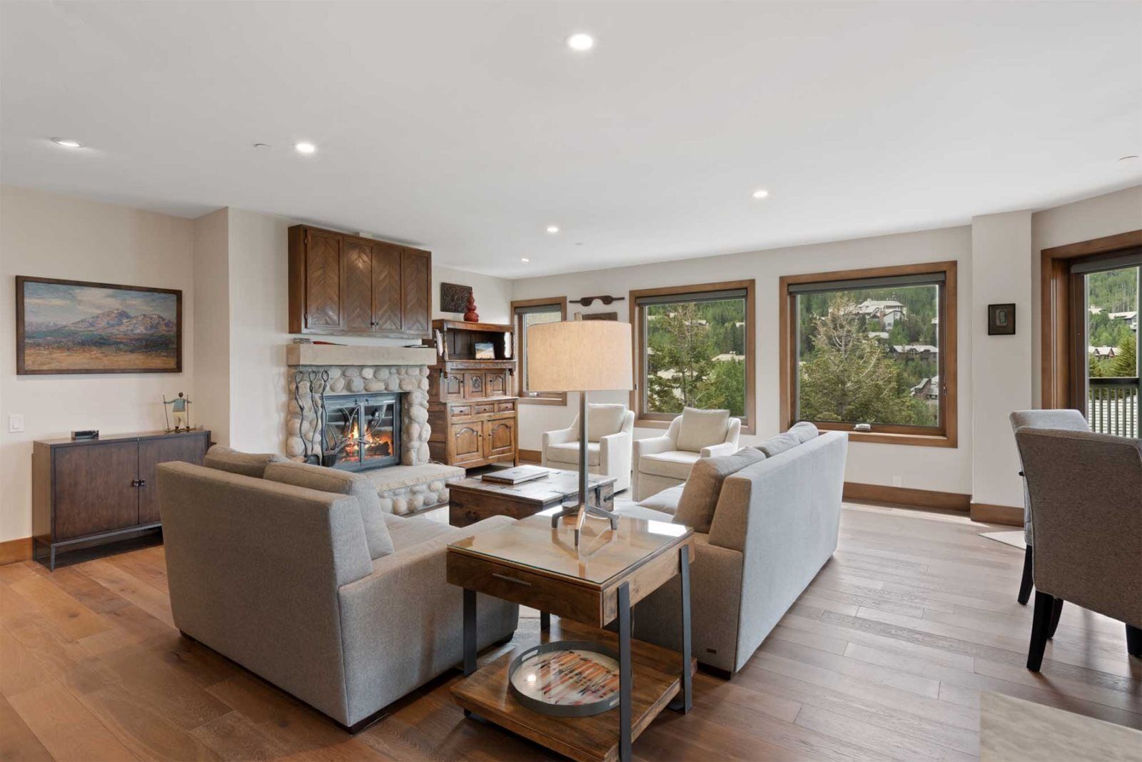 A spacious living room with a fireplace, sofas, a coffee table, and large windows offering a view of the outdoors.