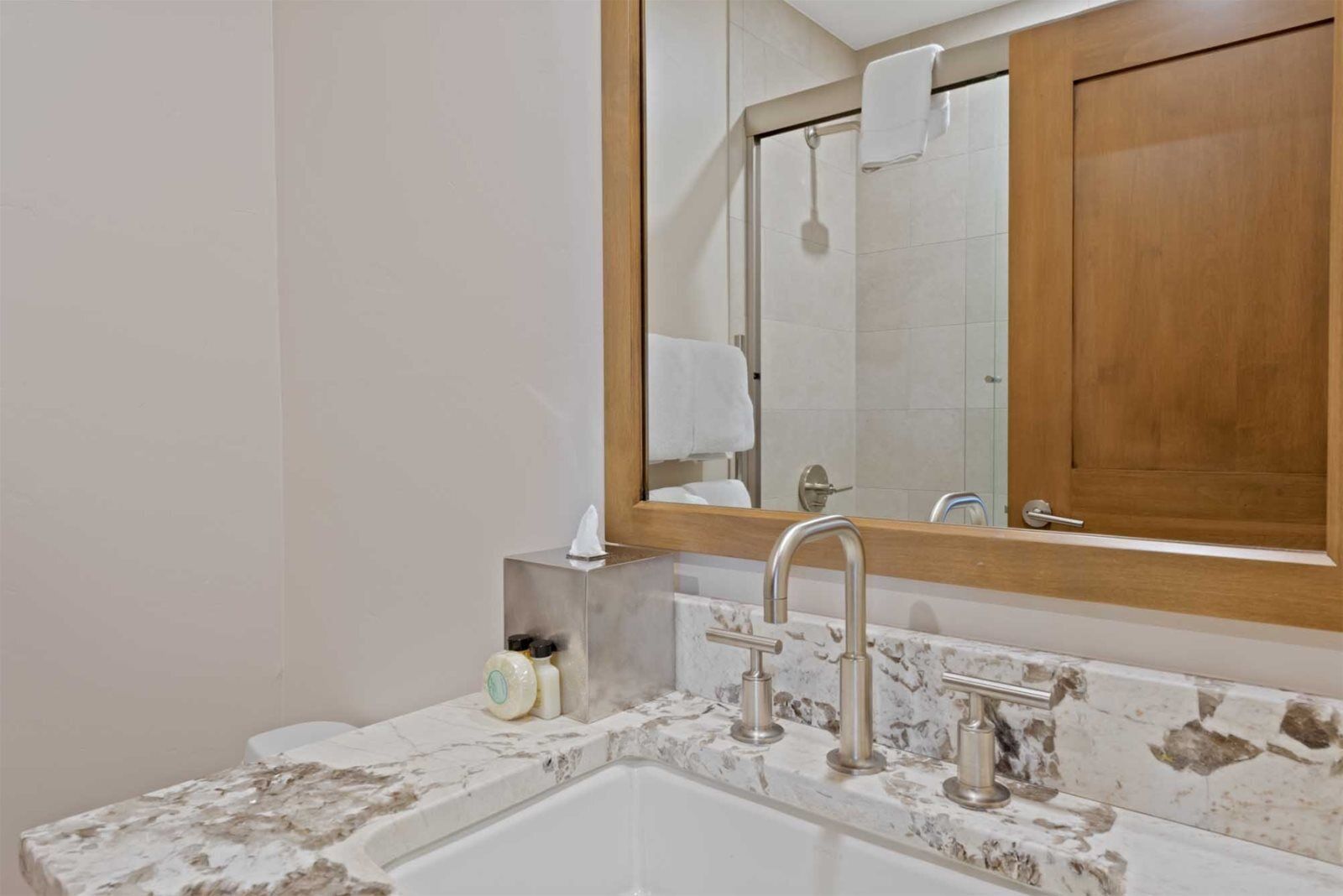 Une salle de bain avec un lavabo en marbre, un miroir encadré en bois et une cabine de douche.