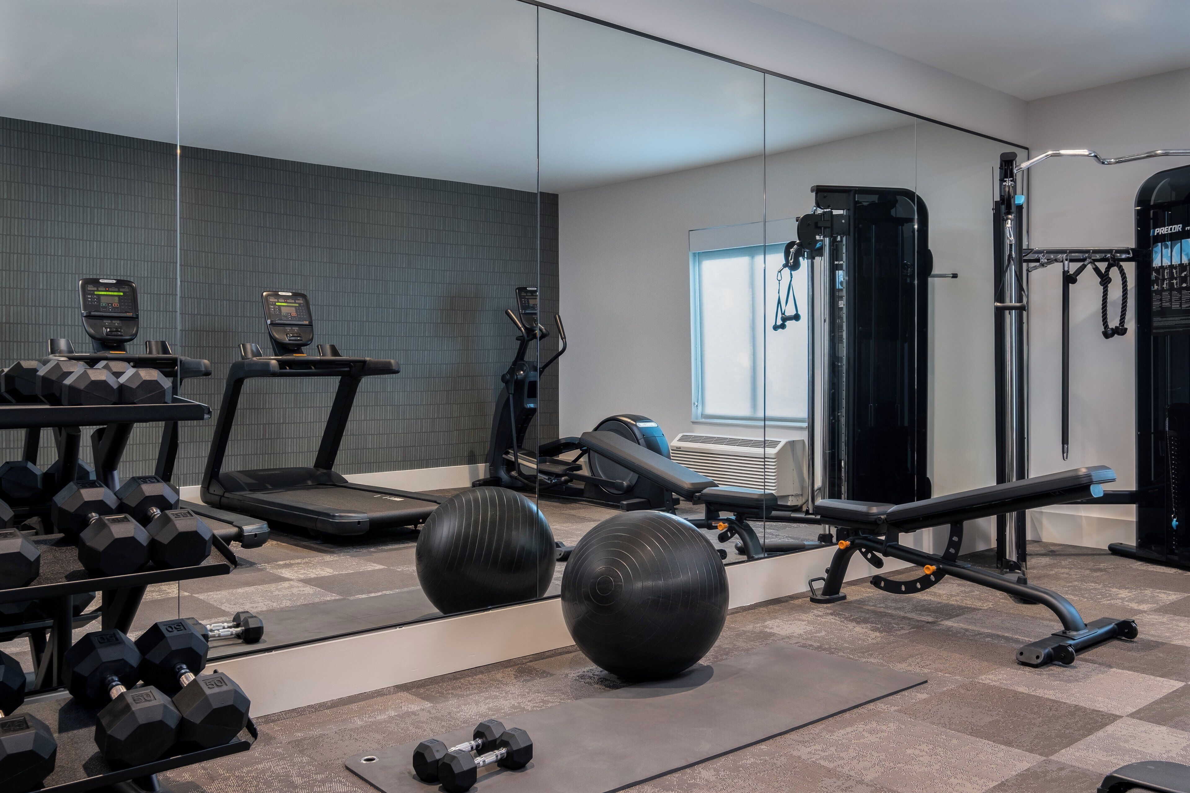 Un gimnasio con cintas de correr, pesas, balones de ejercicio y una estructura para sentadillas.