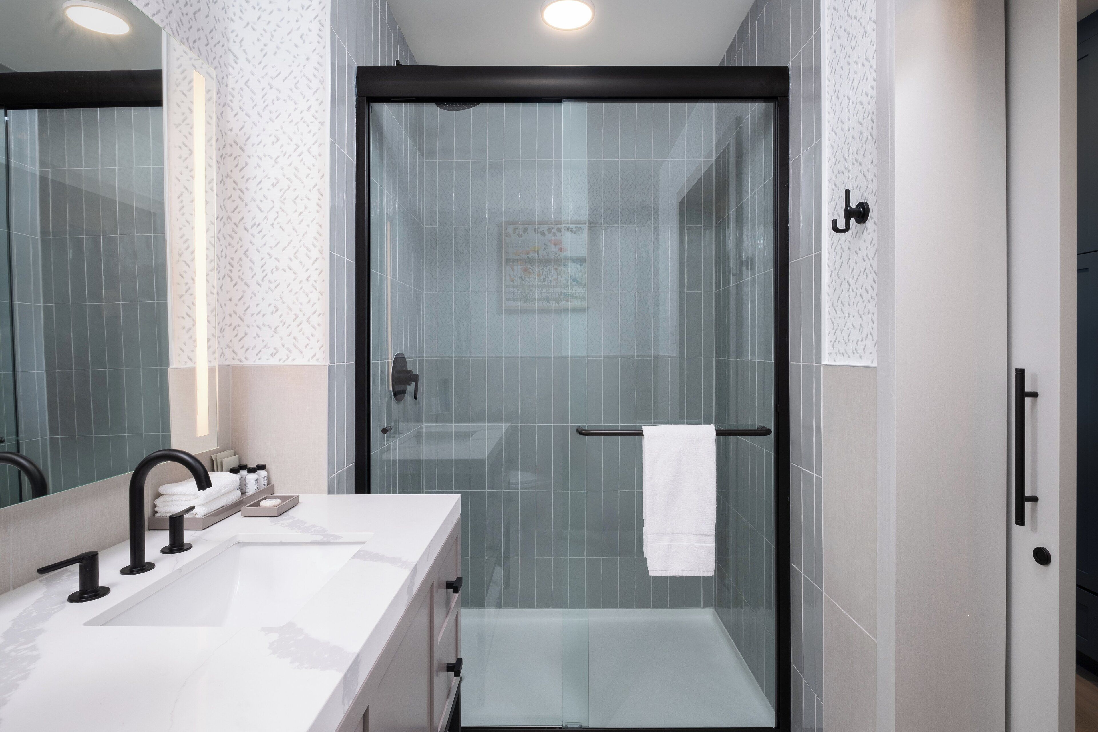 A modern bathroom with a glass-enclosed shower, a white sink with black faucets, and a towel rack.