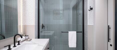 A modern bathroom with a glass-enclosed shower, a white sink with black faucets, and a towel rack.