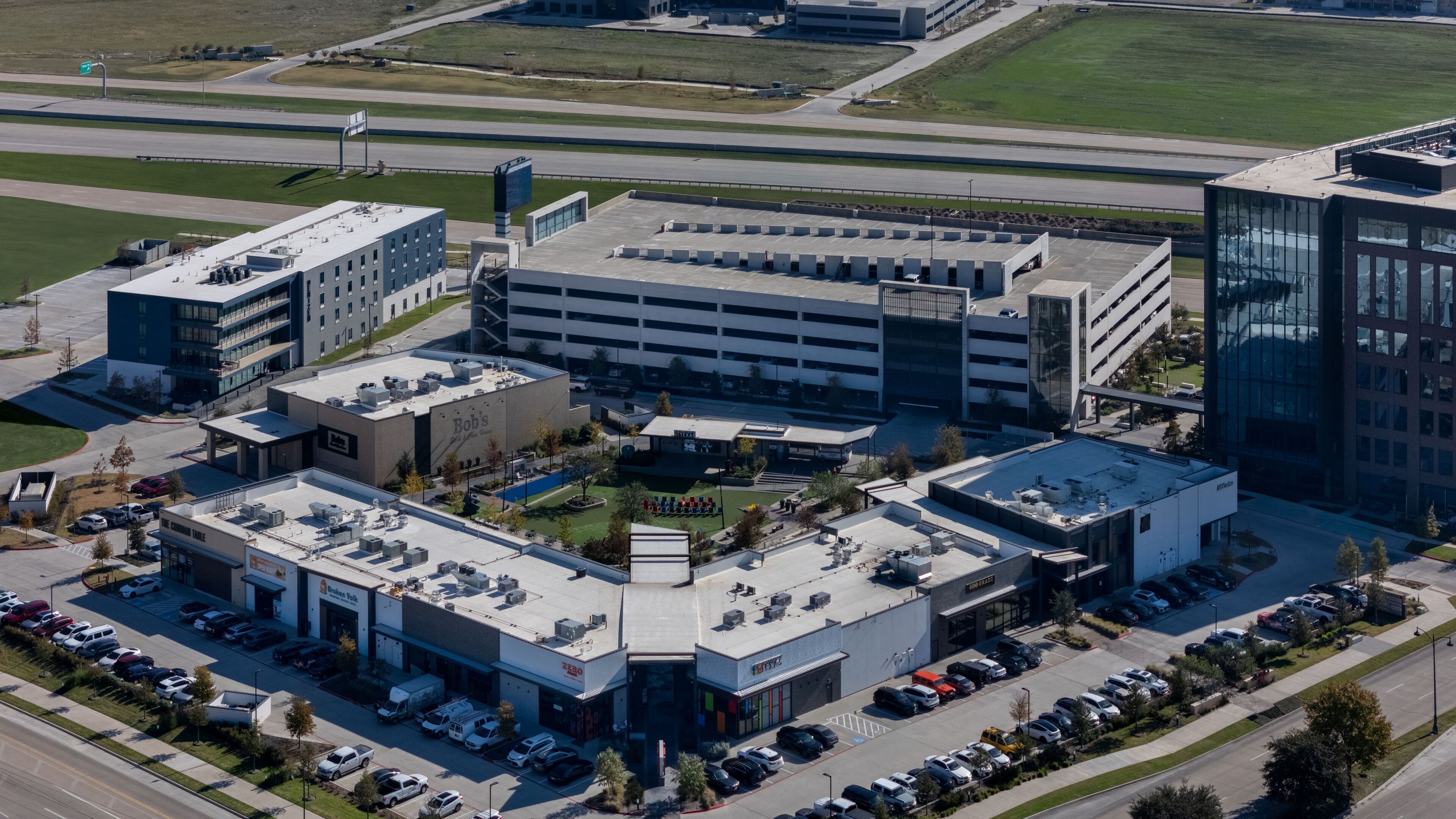 Vue aérienne d’un ensemble immobilier commercial comprenant plusieurs parkings, un parking central en sous-sol et des immeubles de bureaux adjacents.