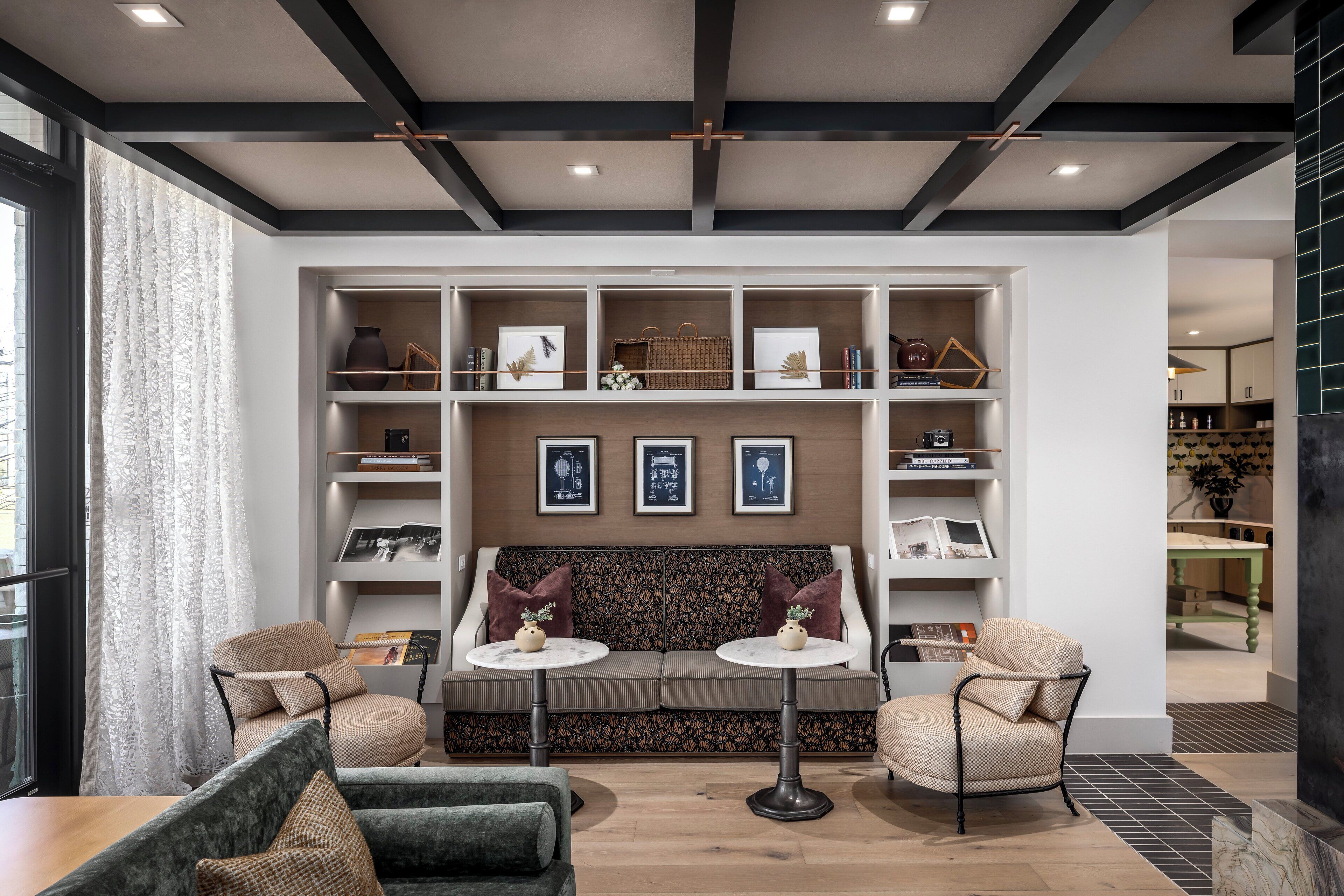 A modern living room with a sofa, two armchairs, a coffee table, and a bookshelf filled with books and decorative items.