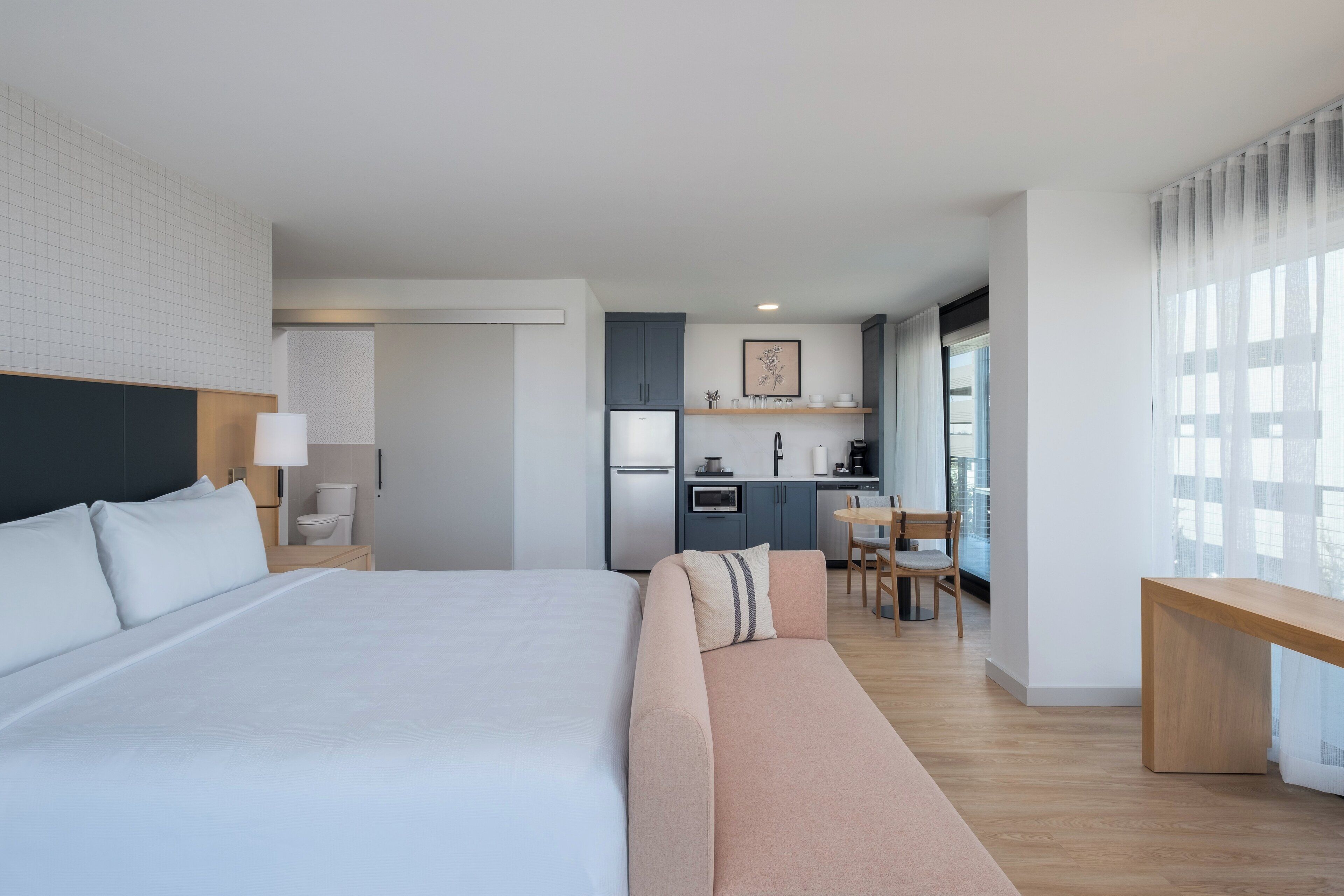 Quarto de hotel moderno com uma cama grande, um sofá, uma pequena cozinha e uma mesa de jantar.