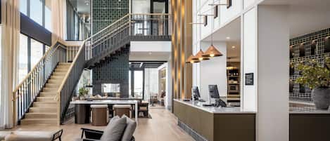 A spacious hotel lobby with a central staircase, a reception desk, and a seating area.