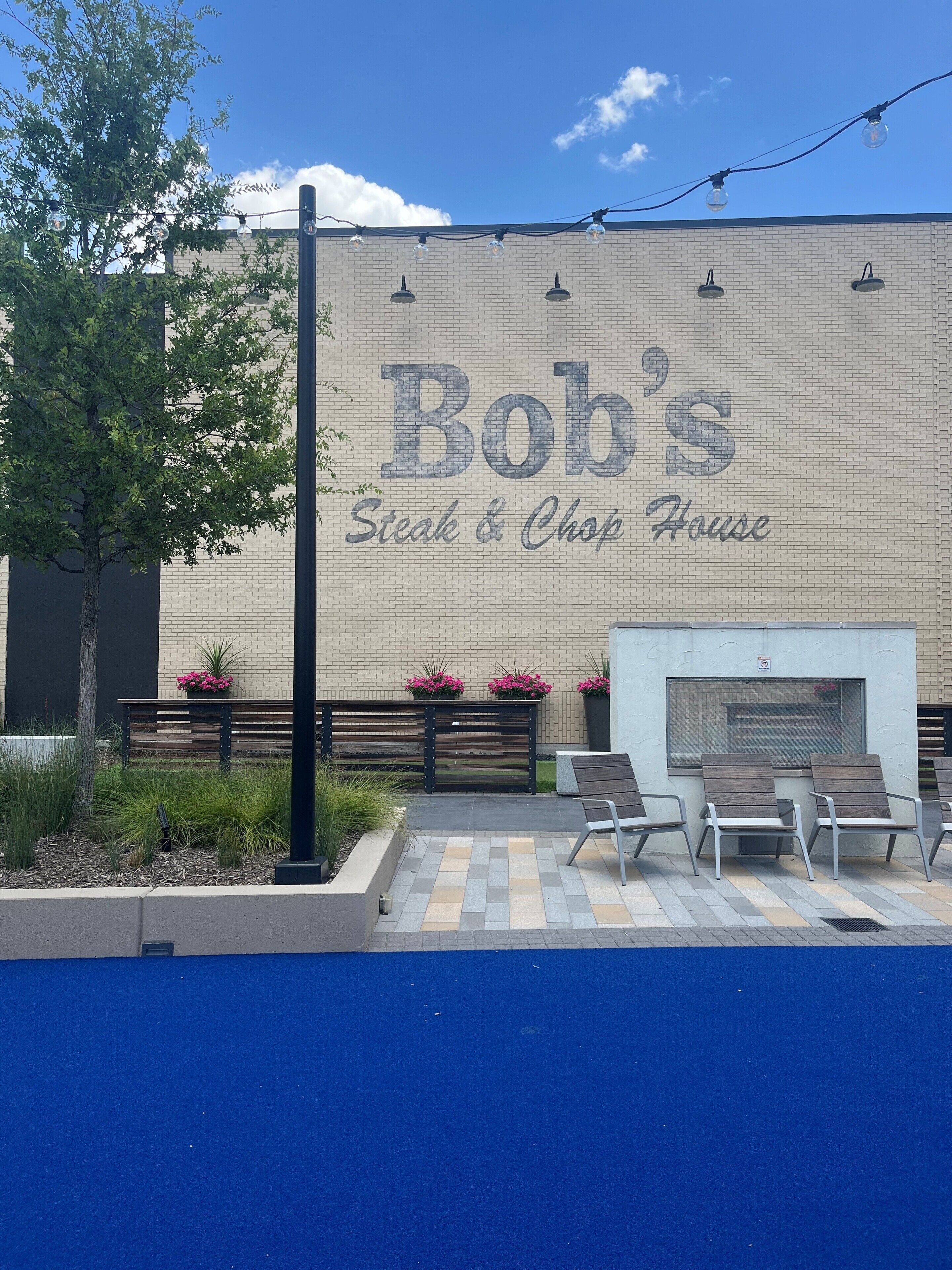 An outdoor seating area with a brick wall, a sign for Bob's Steak & Chop House, and a fire pit.