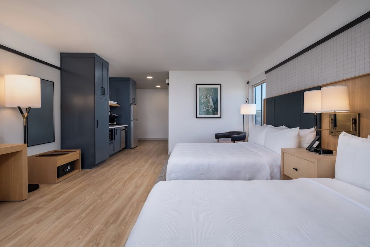 A hotel room with two beds, a desk, a wardrobe, and a painting on the wall.
