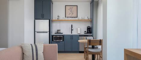 Una cocina moderna con armarios grises, horno empotrado y cafetera. Hay una mesa de comedor con sillas y un sofá con cojines.