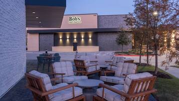 An outdoor seating area with wooden chairs and tables, a brick wall, and a building with a sign that reads "Bob's Steak & Chop House".