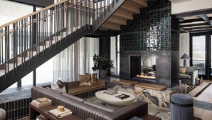 A modern living room with a staircase, a fireplace, and a view of the outdoors. - Denizen Hotel (McKinney)