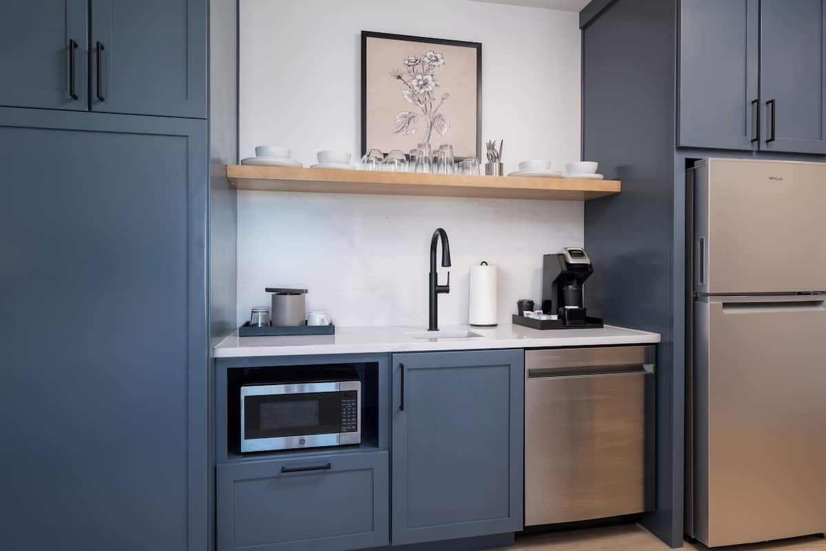 A modern kitchen with grey cabinets, a stainless steel refrigerator, a microwave, and a coffee maker.