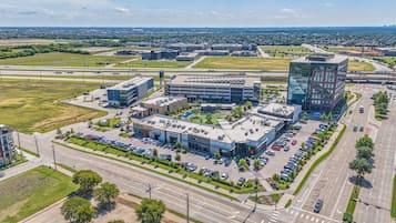 Vista aérea de una zona comercial con estacionamiento, un edificio grande de varios pisos y un edificio más pequeño contiguo.