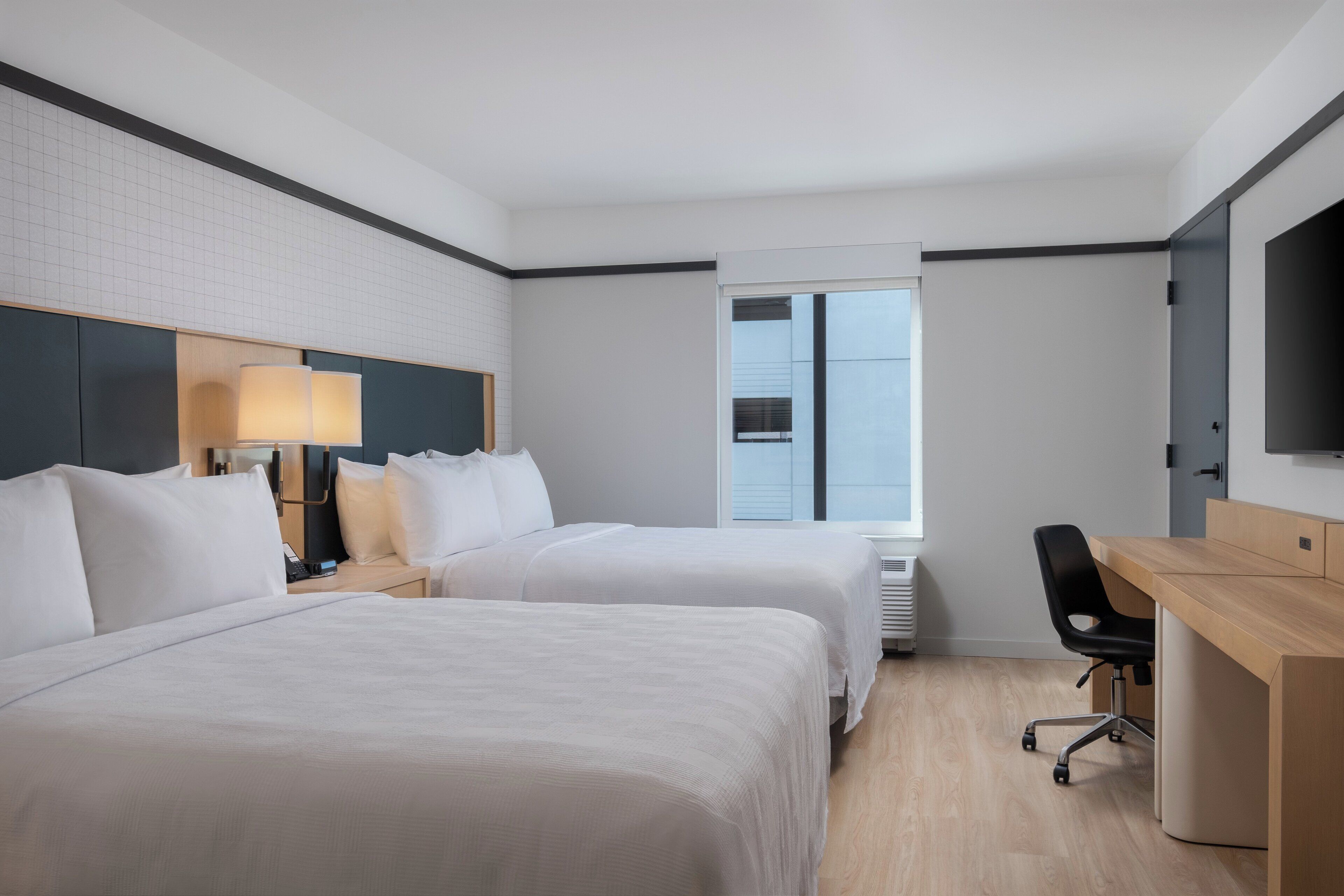 A hotel room with two beds, a desk, a chair, and a TV.
