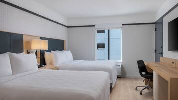 A hotel room with two beds, a desk, a chair, and a TV.