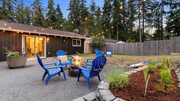 Ein Garten mit Feuerstelle, blauen Adirondack-Stühlen und einer Holzterrasse.
