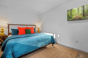 Une chambre à coucher comprenant un lit, des oreillers, des lampes de chevet, un tapis et une décoration murale sur le thème de la forêt.