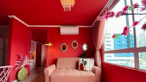 Una habitación con pared roja, sofá rosa, alfombra rosa y una ventana con flores rosadas.