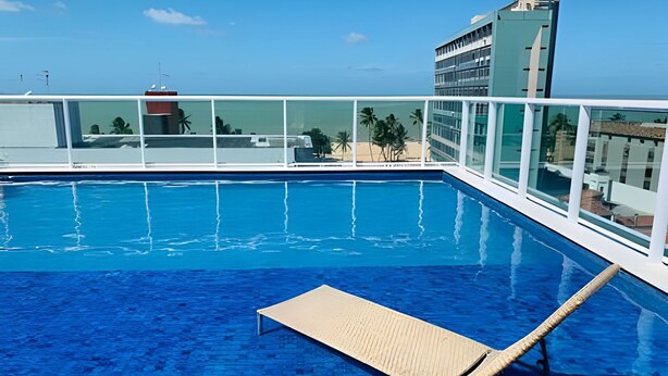 Una piscina en la azotea con agua azul cristalina, una tumbona y vistas al horizonte de la ciudad.