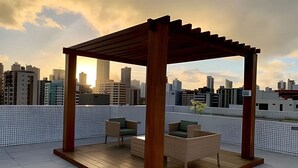Una terraza en la azotea con una pérgola de madera, dos sillones acolchados y una mesita.