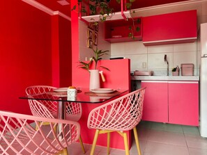 A kitchen with pink cabinets, a glass table, and wicker chairs. - O Apartamento Rosa (João Pessoa)