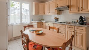 Une cuisine avec des meubles de rangement en bois, une table à manger avec des chaises, une fenêtre avec des rideaux et un luminaire suspendu.