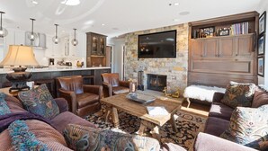 A spacious living room with a stone fireplace, leather sofas, a wooden coffee table, and a flat-screen TV mounted on the wall. - Beaver Creek Residences - 2 Bedroom Luxury Ski In/out Condo (Avon)