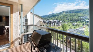 A balcony with a grill, a view of a mountainous landscape, and a building with multiple balconies. - Beaver Creek Residences - 2 Bedroom Luxury Ski In/out Condo (Avon)