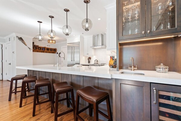 Una cocina moderna con una isla grande, taburetes de bar, electrodomésticos de acero inoxidable e iluminación colgante.