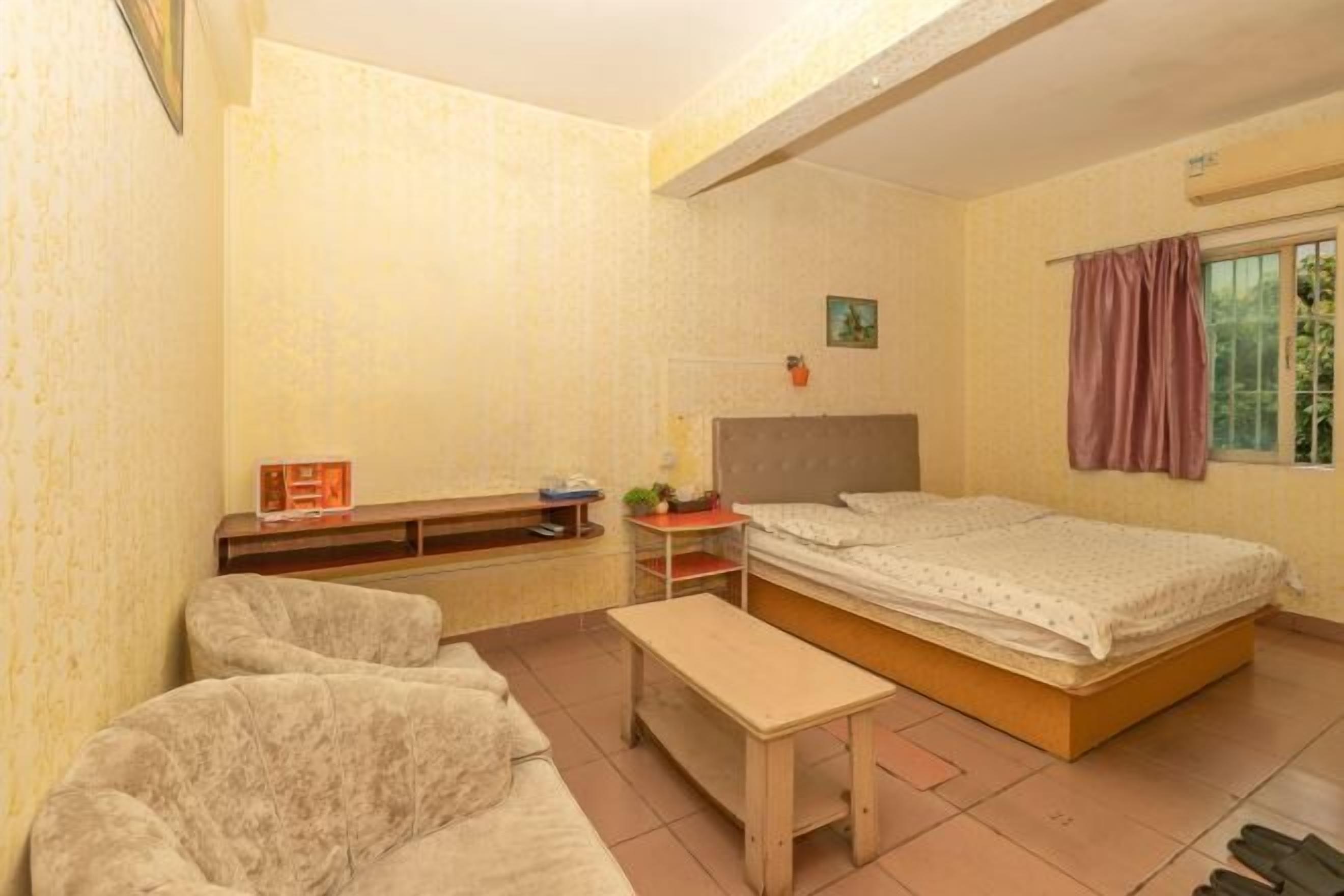 A small, well-lit room with a bed, a sofa, a small table, and a window with curtains.