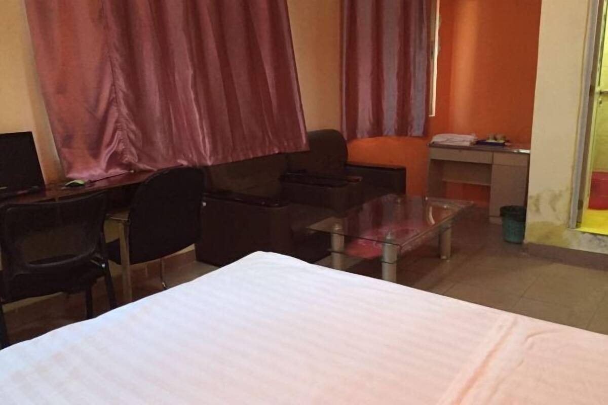 A hotel room with a bed, a desk, a chair, a small table, and a glass partition.