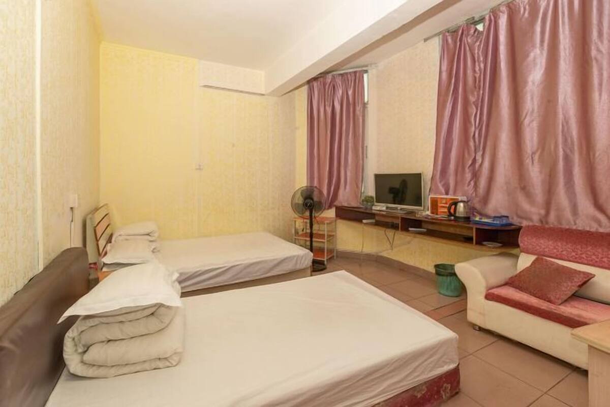 A room with two beds, a sofa, a TV, and a desk with a computer.