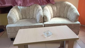 A beige sofa with a glass coffee table in a room with a tiled floor and a red curtain.