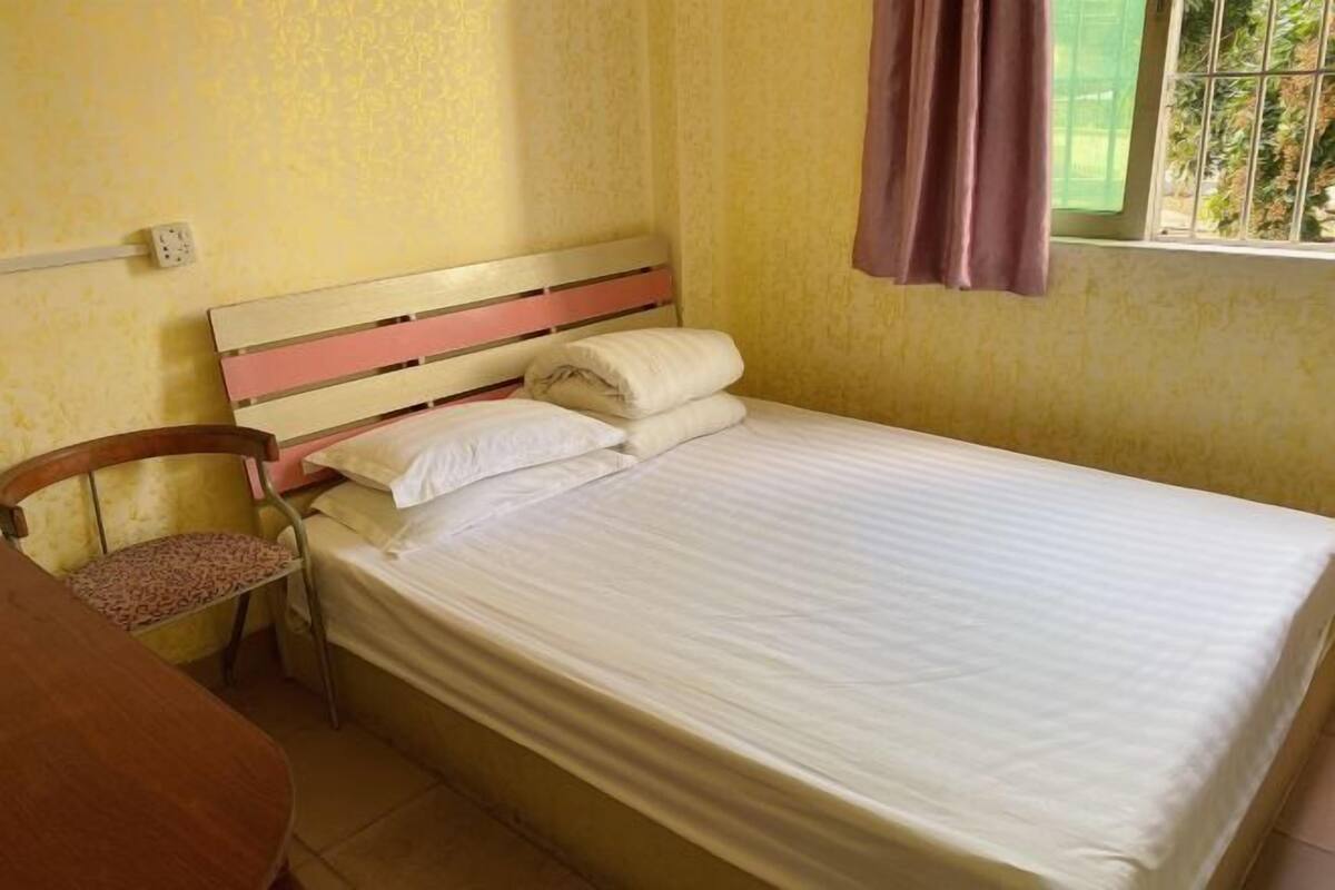 A single bed with a wooden headboard, a chair, and a window with curtains.