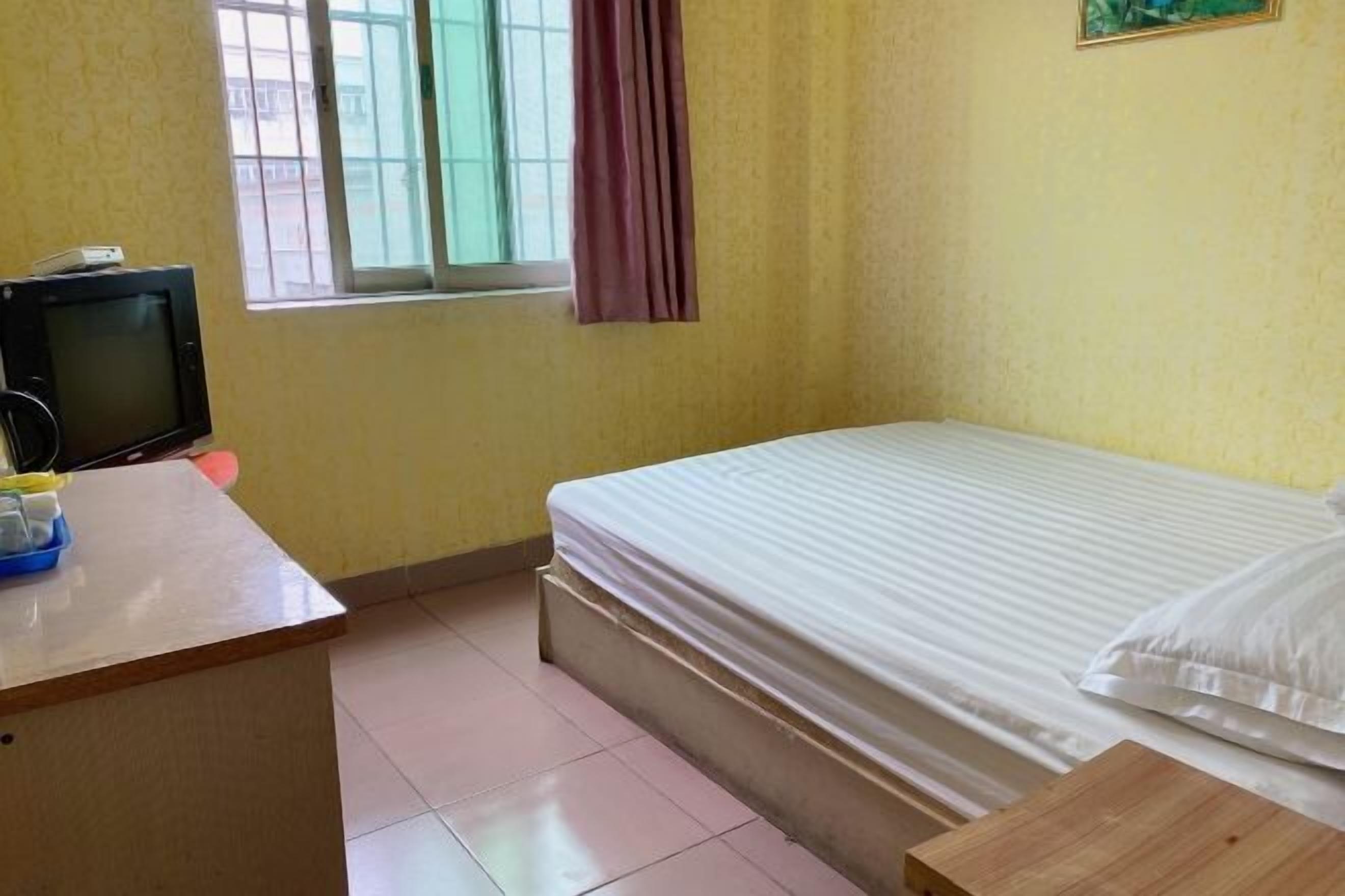 A room with a bed, a desk with a computer, a window with curtains, and a small table.