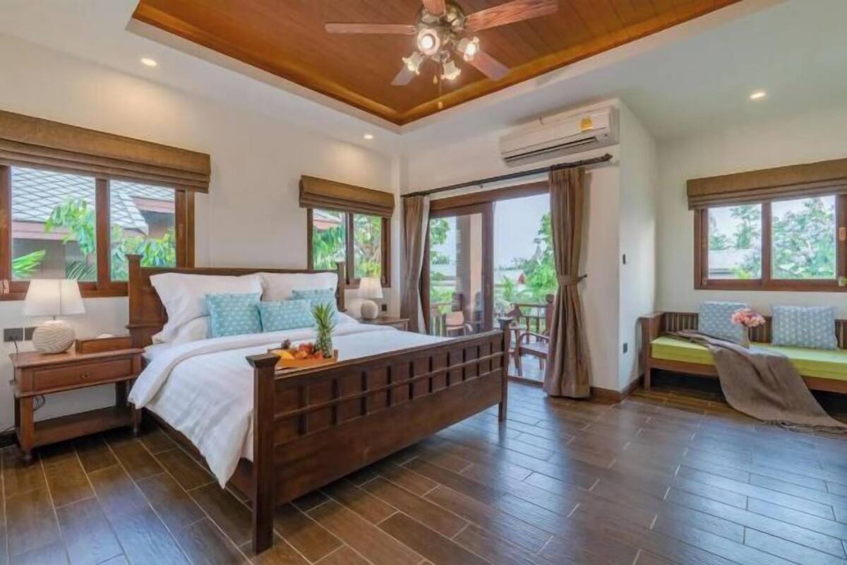 A bedroom with a wooden bed, a nightstand, a ceiling fan, and large windows.