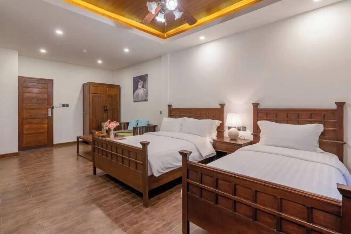 A hotel room with two wooden beds, a ceiling fan, recessed lighting, and a wooden wardrobe.