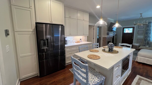 A modern kitchen with white cabinetry, a black refrigerator, and a central island with seating. - Charming Game Day House  (Opelika)