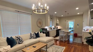 A spacious living room with a large sectional sofa, a wooden coffee table, and a chandelier. - Charming Game Day House  (Opelika)