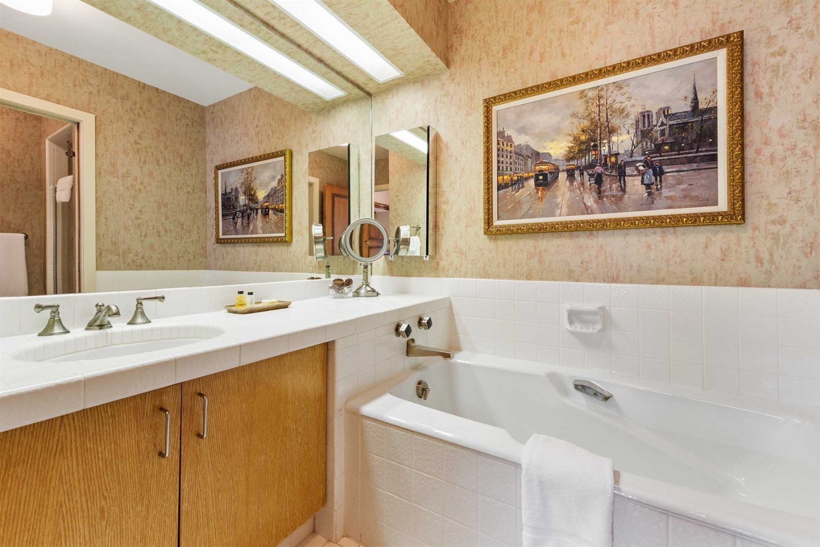 A bathroom with a large bathtub, a double sink vanity, and two framed paintings on the wall.