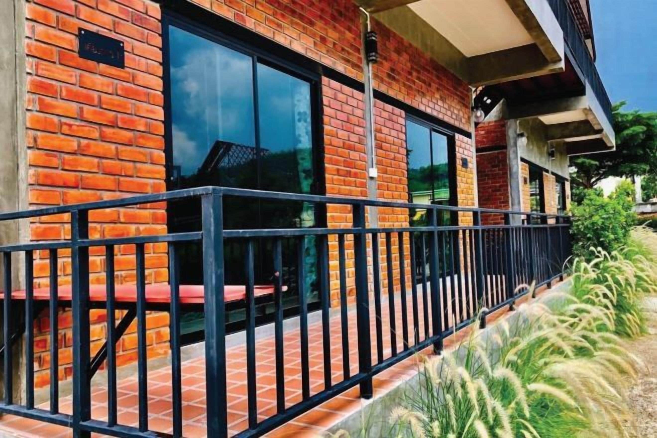 A brick building with large windows, a black metal railing, and a small outdoor seating area.