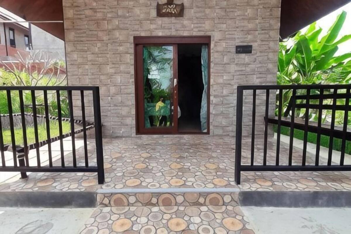 A building entrance with a stone-tiled ground, a wooden door, and a black metal gate.