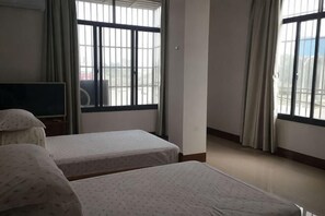 A hotel room with two beds, a TV, and large windows with curtains.