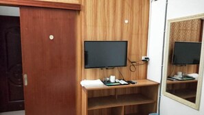 Een kamer met een houten wand, een aan een plank bevestigde televisie, een spiegel en een deur.