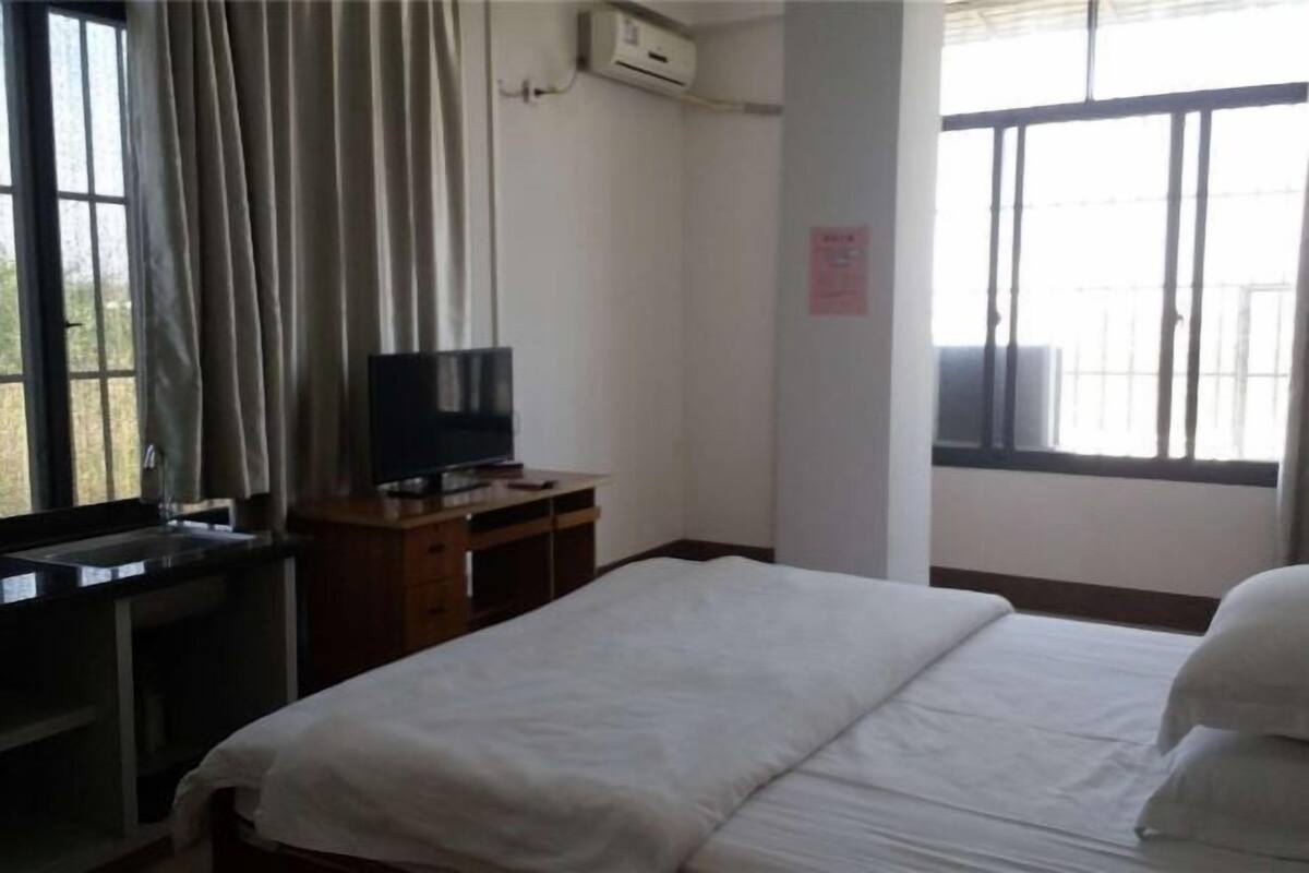 Habitación de hotel con una cama, un televisor sobre un mueble de madera, una ventana con cortinas y un equipo de aire acondicionado en la pared.