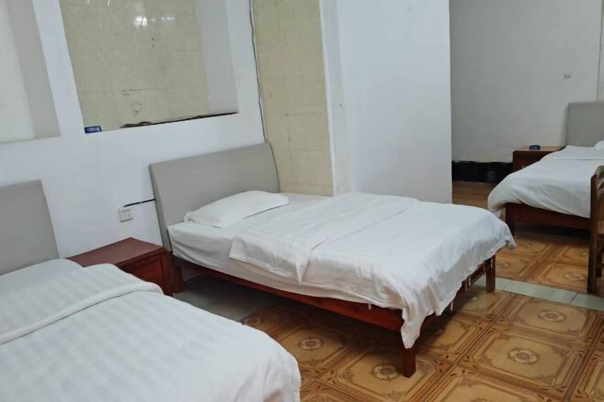 Habitación de hotel con dos camas individuales, piso de madera, una mesita de noche de madera y una pared lisa con una ventana.